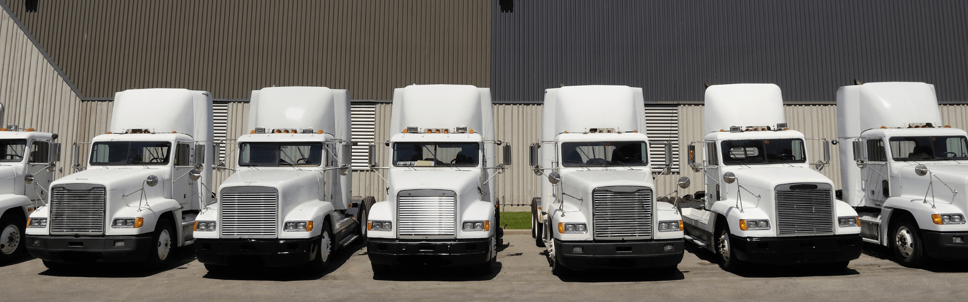 white semi trucks parked in a line in front of a warehouse