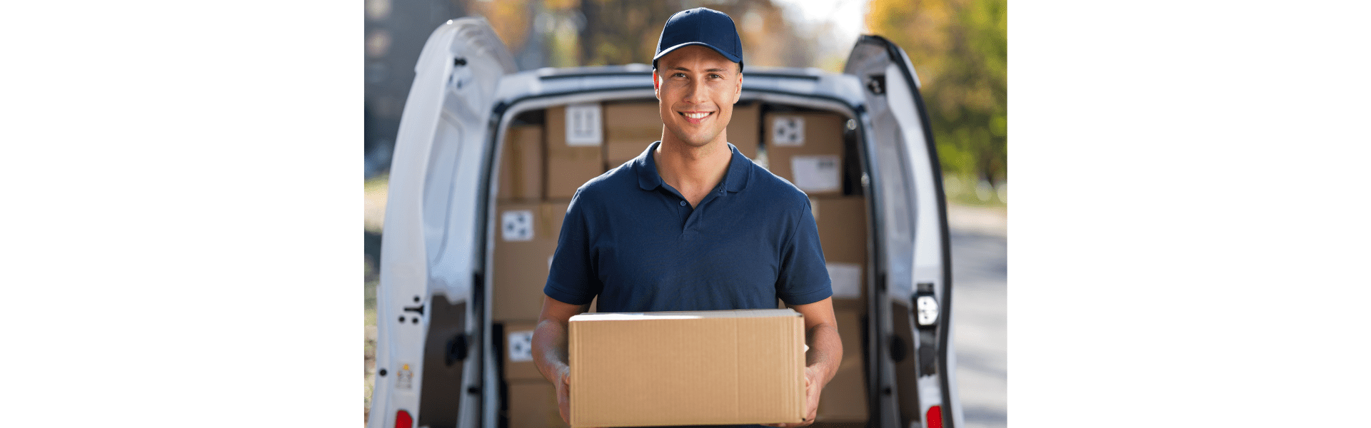 man in hat and polo shirt holding box standing in front of a delivery van full of packages with the rear doors open