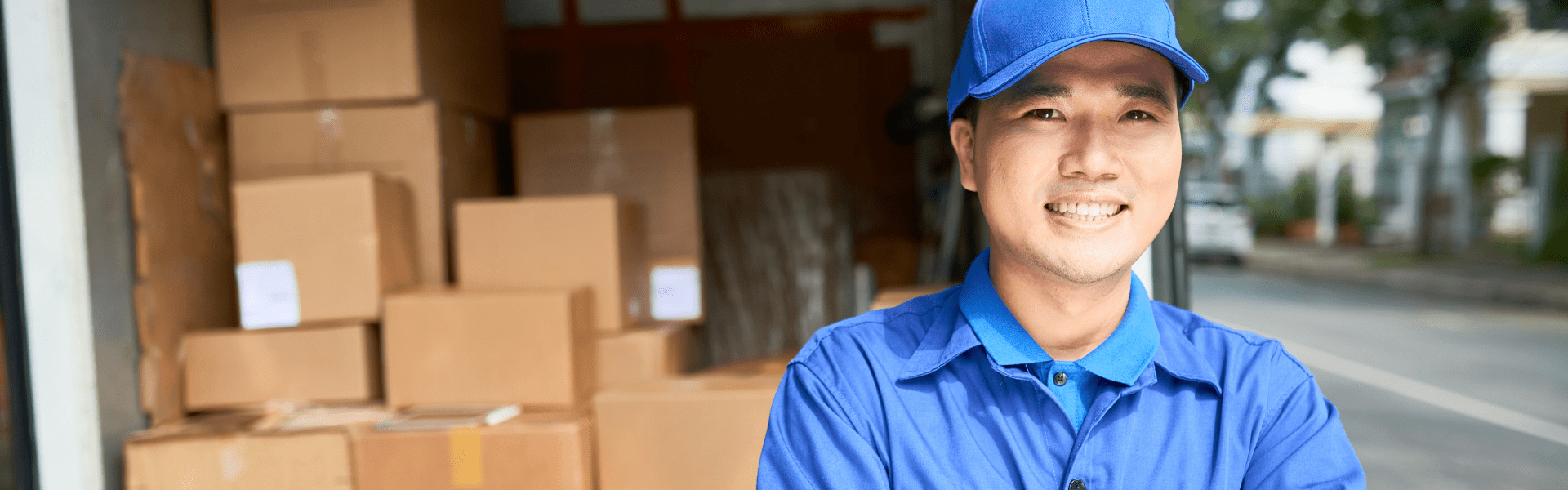 man in blue polo and blue hat standing in front of a delivery van with the back doors open revealing stacked packages inside