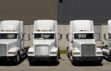 white semi trucks parked in a line in front of a warehouse