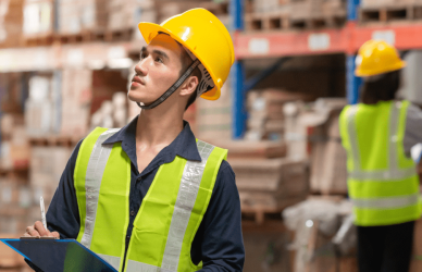 workers with yellow safety vests and hard hats holding clipboards in warehouse full of boxes, NYC microhub for final mile deliveries