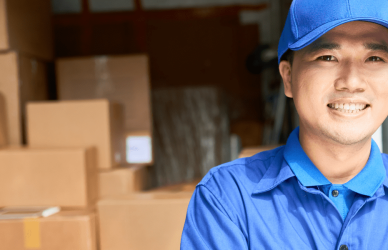 man in blue polo and blue hat standing in front of a delivery van with the back doors open revealing stacked packages inside